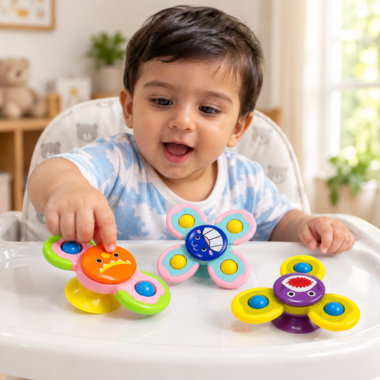 A baby sitting in a high chair at a white table tray, playing with colorful spinner toys. The baby is wearing a light blue and white cloud-patterned t-shirt.